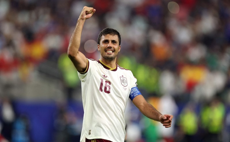 Soccer player in a white jersey number 16 raises his fist in celebration on the field.