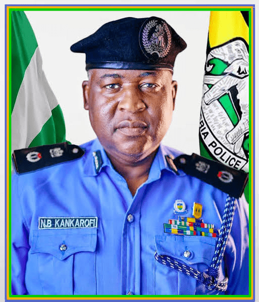 Kogi Commissioner of Police,CP Naziru Bello Kankarofi - THEWILL NEWS MEDIA Portrait of a Nigerian police officer in a blue uniform with name tag N.B. KANKAROFI, wearing a beret, medals, and flags in the background.