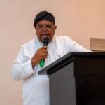 FG Sets 2027 Deadline to End Power Subsidies, Rules Out Immediate Tariff Hike Man wearing a white traditional outfit and black cap speaks into a microphone at a podium in a formal setting.