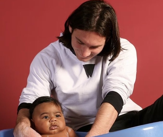 An iconic UNICEF charity photograph taken in 2007 shows a young Lionel Messi bathing six-month-old Lamine Yamal Photo: Joan Monfort/UNICEF/Sport. Caregiver washing a baby in a blue tub against a red background, focusing on bath time care