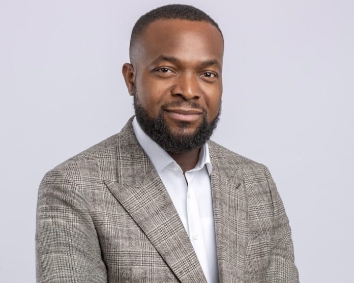 Professional headshot of a smiling man in a gray plaid blazer and white shirt, neutral background.