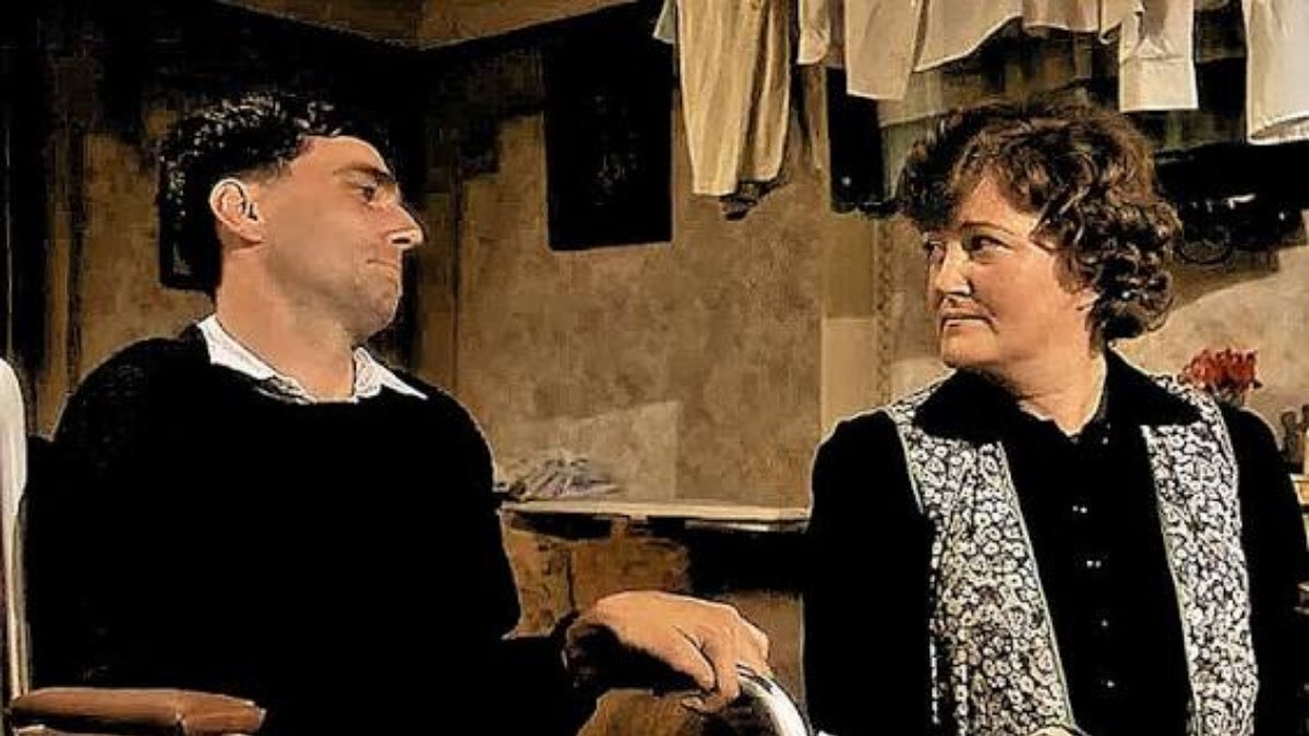 Brenda Fricker with Daniel Day-Lewis in My Left Foot (1989). Credit: IMDb - THEWILL NEWS MEDIA Two adults sit in a rustic room, facing each other; man on the left wears black, woman on the right has a patterned vest and dark top.
