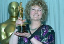 Brenda Fricker, Oscar Winner and ‘Home Alone 2’ Star, Dies at 81 Smiling woman with curly hair holding an Oscar trophy in front of a gold statuette backdrop.