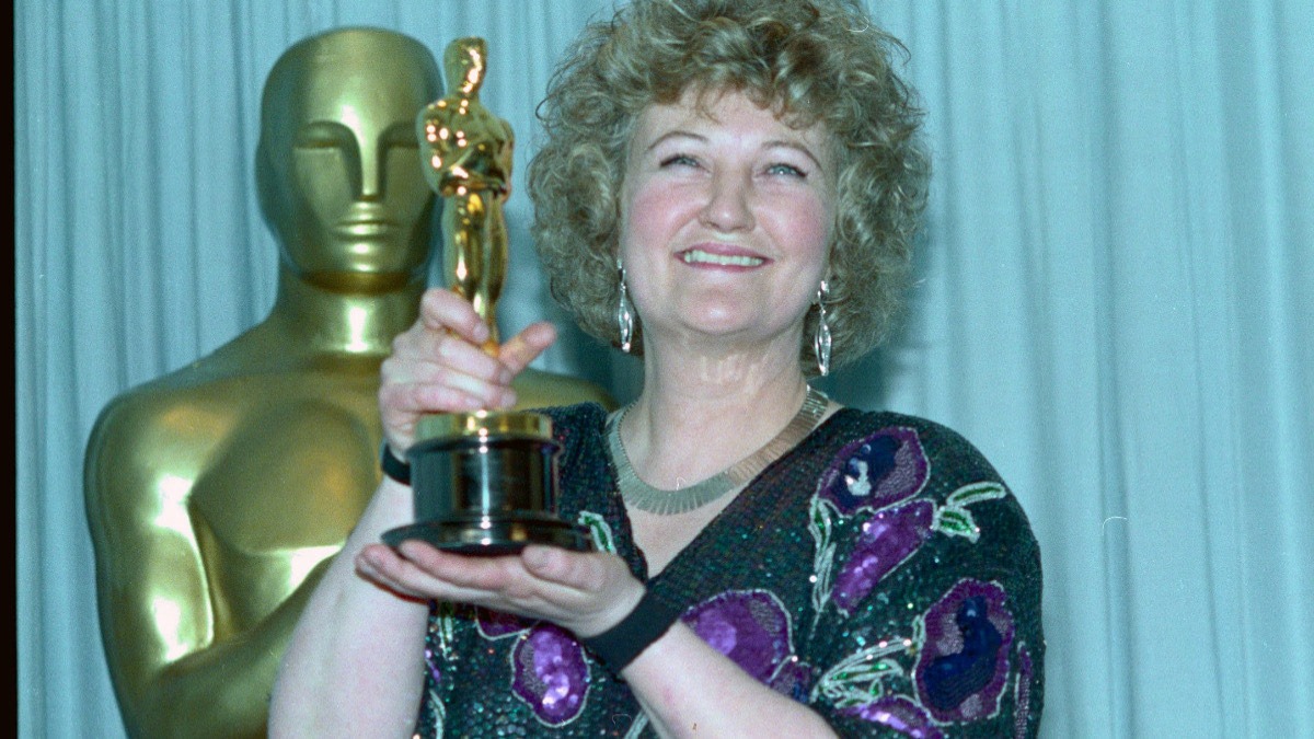Brenda Fricker with her Oscar after winning Best Supporting Actress for My Left Foot. Credit: Bettmann - THEWILL NEWS MEDIA Smiling woman with curly hair holding an Oscar trophy in front of a gold statuette backdrop.