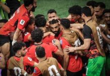 Egypt Make History, Beat Australia on Penalties To Reach First Ever World Cup Last 16 Soccer players in red jerseys form a tight huddle, celebrating on the field after a match.