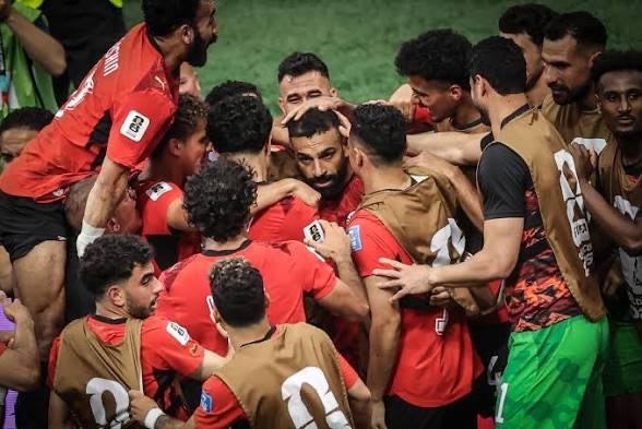 Soccer players in red jerseys form a tight huddle, celebrating on the field after a match.