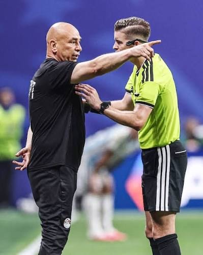 IMG_6653 Soccer coach in black shirt argues with a neon-yellow referee on the field, pointing emphatically.