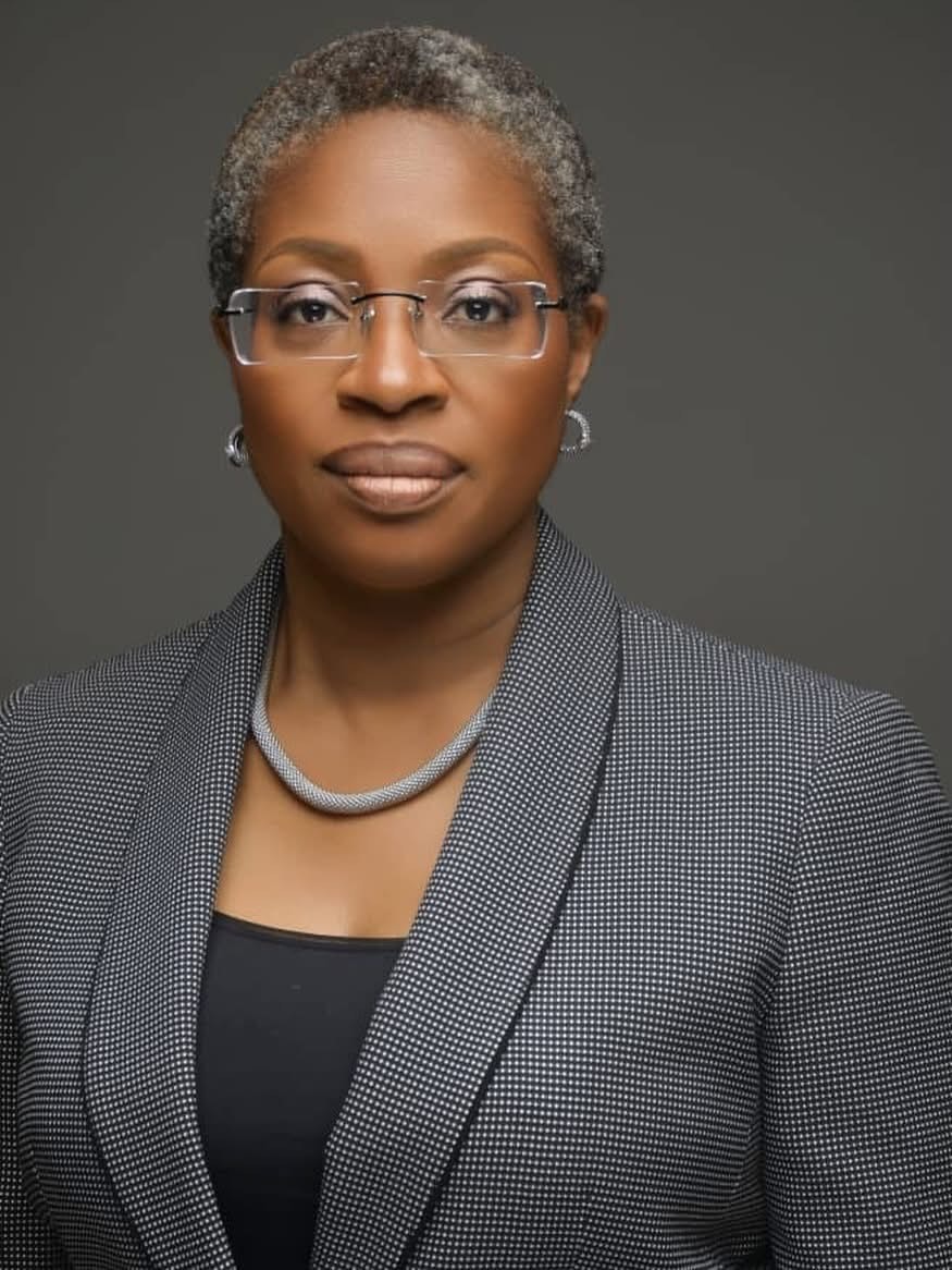 Professional headshot of a Black woman with short gray hair, glasses, a gray checkered blazer, and a silver necklace.