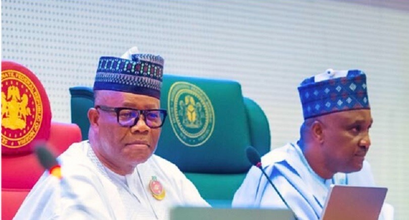 Senator Akpabio - THEWILL NEWS MEDIA Two men in traditional white agbada and caps sit at a panel with microphones; official logos on the chairs behind them.