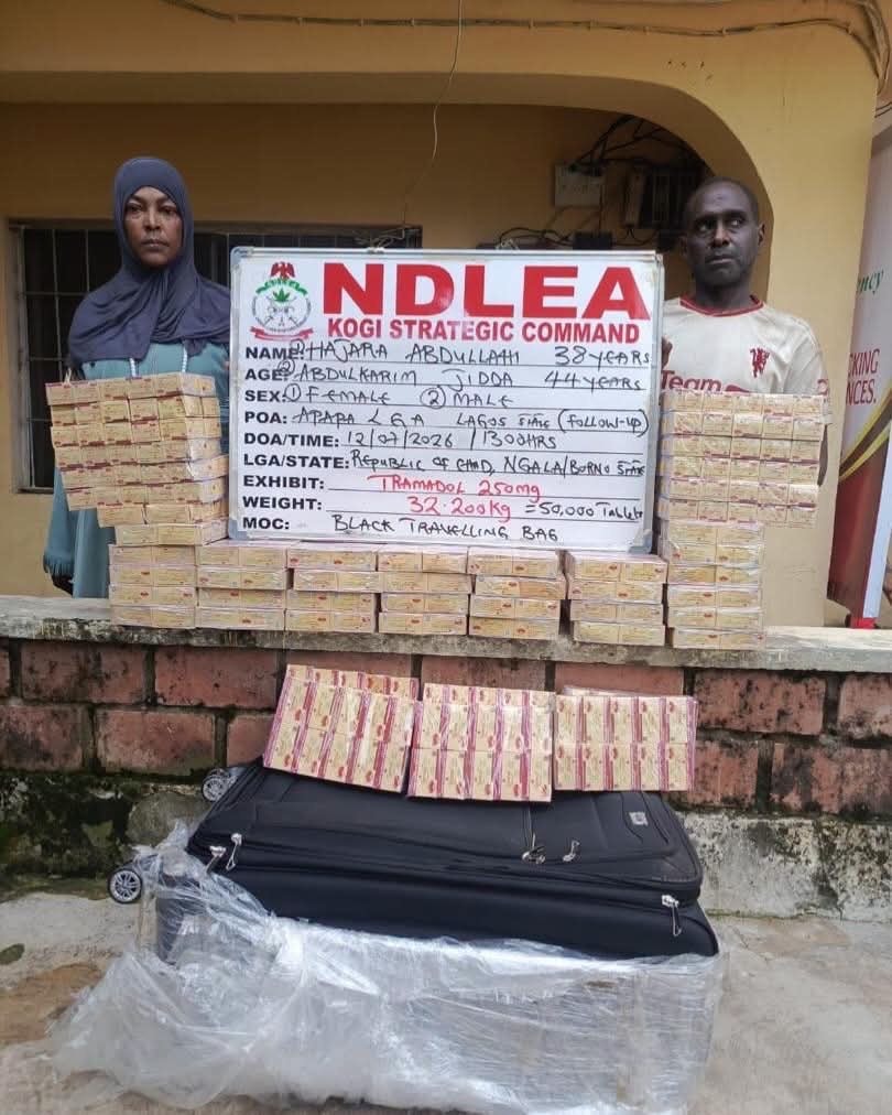 NDLEA Hajara Abdullahi - THEWILL NEWS MEDIA Two individuals stand beside a white NDLEA Kogi Strategic Command display board, flanked by stacked rectangular packages and a large suitcase on plastic wrap, suggesting a seized drug haul.
