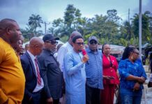 AKHA Oversight Committee Gives Itu Council Clean Bill On Projects, Accountability Man in a light blue traditional outfit speaks into a red microphone at an outdoor gathering, surrounded by a diverse group of people.