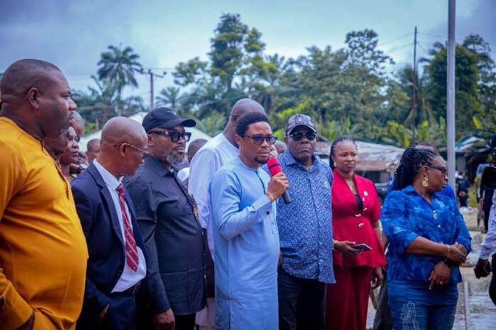 Itu Local govt council Man in a light blue traditional outfit speaks into a red microphone at an outdoor gathering, surrounded by a diverse group of people.