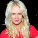 British Singer Lauren Bennett, Known for Vocals on “Party Rock Anthem,” Dies at 36 Blonde woman wearing a pink top poses for the camera at a nighttime event on a dark background with lights.