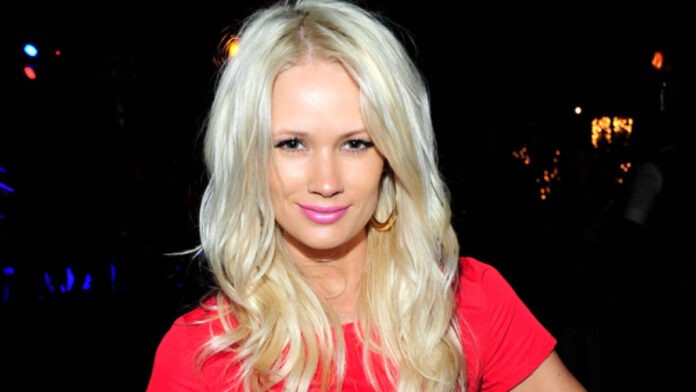 Lauren Bennett Blonde woman wearing a pink top poses for the camera at a nighttime event on a dark background with lights.