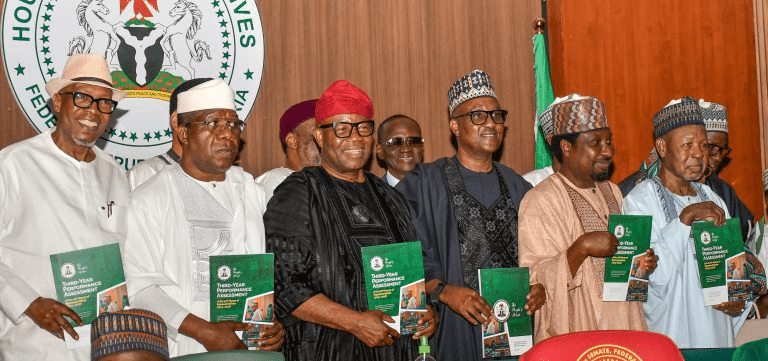 NASS - THEWILL NEWS MEDIA Group of Nigerian officials in traditional and formal attire, each holding a green report booklet at a formal event in front of a government seal backdrop.
