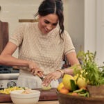 Duchess Of Sussex Meghan Markle Scores First Daytime Emmy Nomination For Netflix Series ‘With Love, Meghan’ Woman chopping an onion on a wooden cutting board in a bright kitchen, with herbs and a basket of fruit nearby