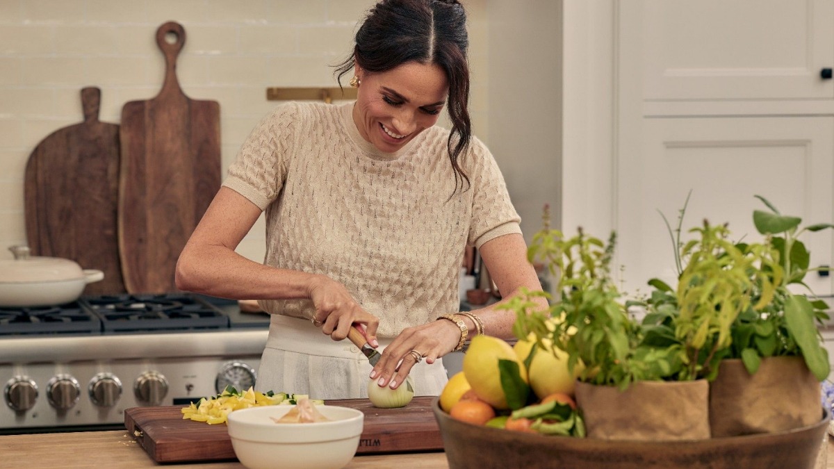 Meghan Markle, Duchess of Sussex. Credit: Chris Jackson/Getty Images | ‘With Love, Meghan’ Netflix poster. Credit: Meghan via Instagram - THEWILL NEWS MEDIA Woman chopping an onion on a wooden cutting board in a bright kitchen, with herbs and a basket of fruit nearby