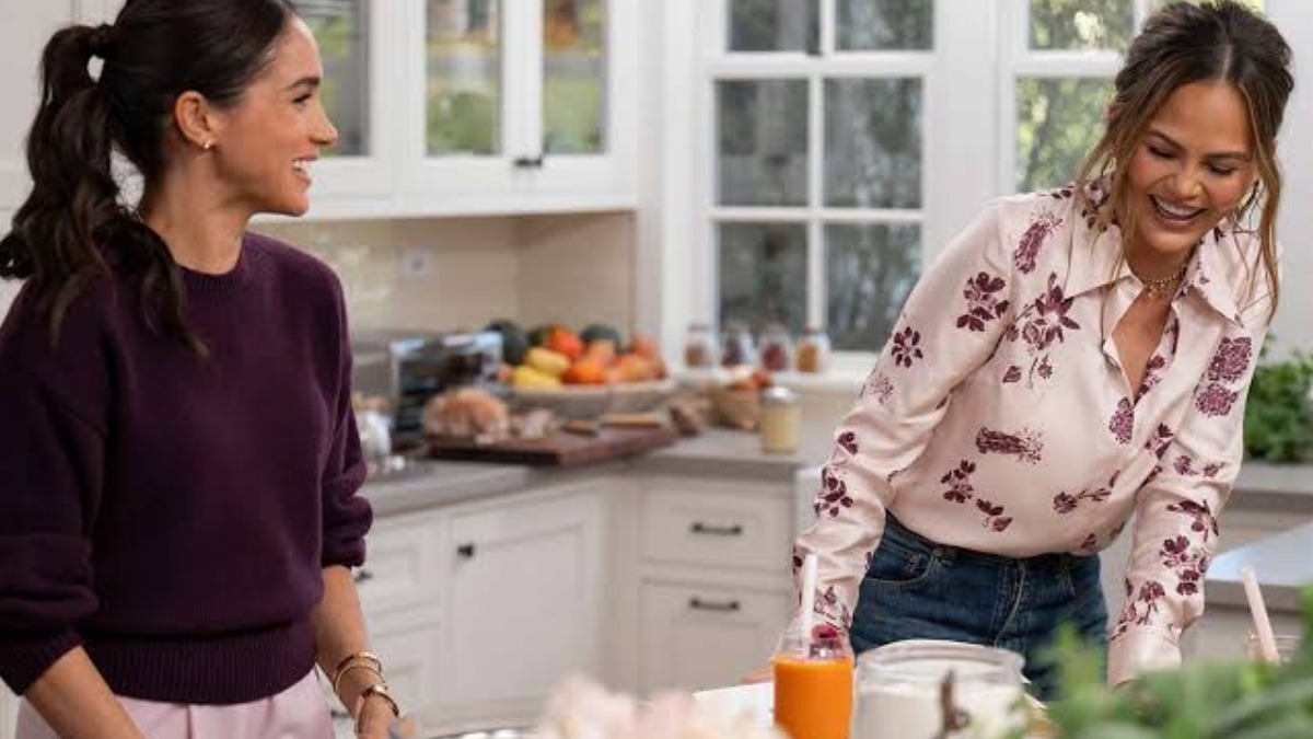 Meghan Markle and Chrissy Teigen on 'With Love, Meghan.' Credit: Jake Rosenberg/Netflix - THEWILL NEWS MEDIA Two women smile and chat in a bright kitchen as they prep drinks, with fruit on the counter and an orange juice bottle nearby.