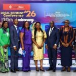 Expert Seeks Stronger Oil, Insurance Alliance to Deepen Local Content Group of eight professionals in formal attire posing for a photo at the Local Content Conference ’26 anniversary backdrop with event banners and logos.