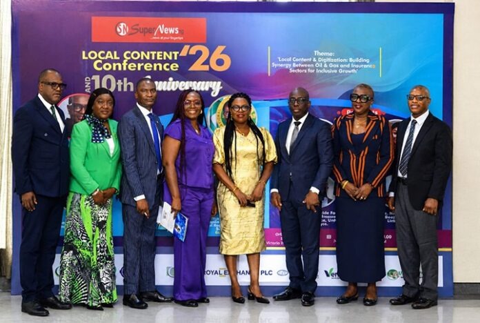 Group of eight professionals in formal attire posing for a photo at the Local Content Conference ’26 anniversary backdrop with event banners and logos.