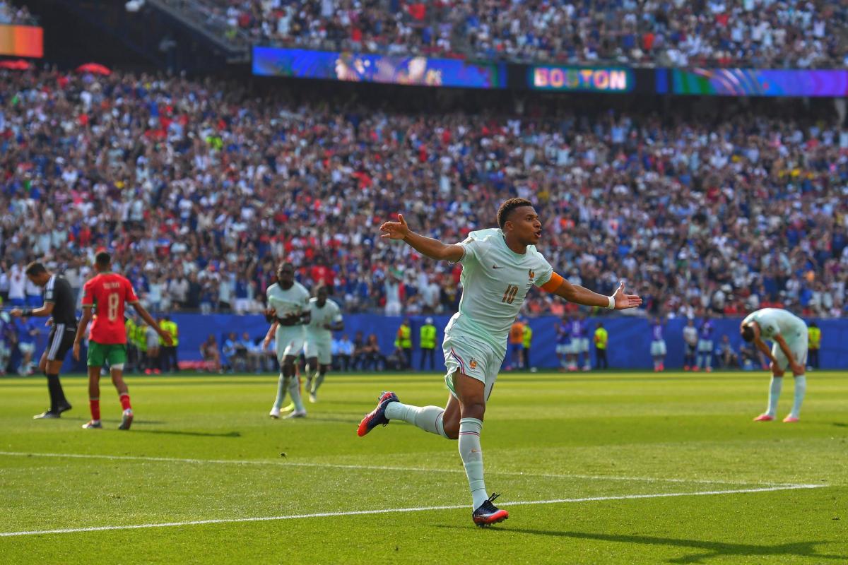 France vs Morocco - THEWILL NEWS MEDIA Soccer player in white number 10 celebrates a goal, arms outstretched on a green field with a cheering crowd.