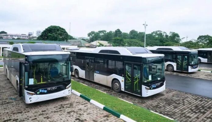 Attached: Pic of some of the CNG buses parked in Government House, Uyo Row of white public transit buses parked in a paved lot with a grassy divider and trees in the background.