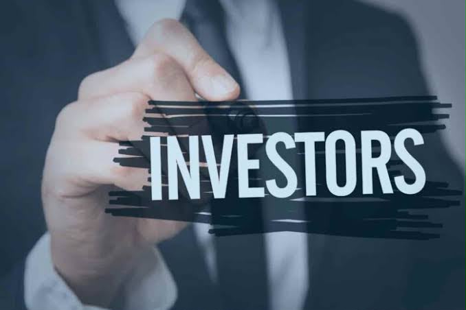 investors - THEWILL NEWS MEDIA Hand overlaying the word INVESTORS on a dark glass panel with brush-stroke accents, suggesting finance or investment topics.