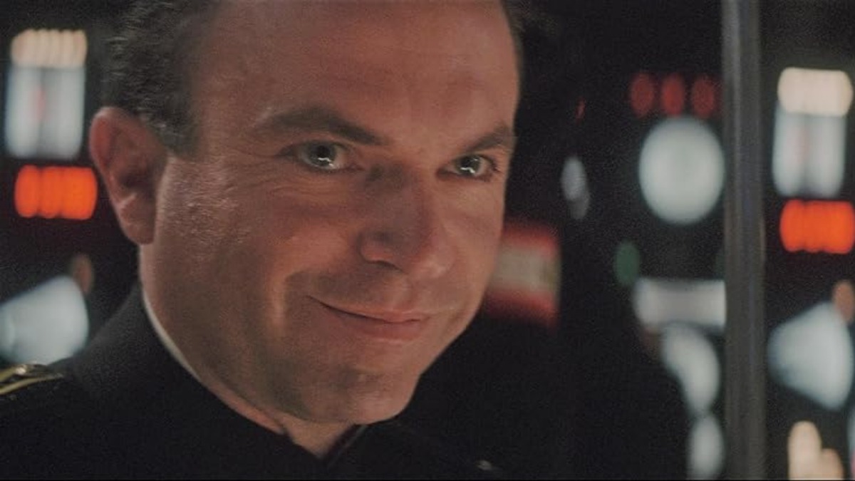 sam neill 4 - THEWILL NEWS MEDIA Smiling man in a dark uniform on a starship bridge with illuminated control panels behind him.