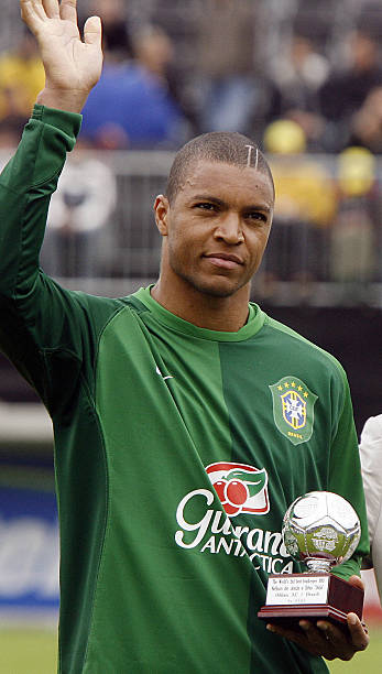 DIDA - THEWILL NEWS MEDIA Brazilian soccer player in a green Brazil jersey raises his right hand and holds a trophy with a football on top on the stadium field.