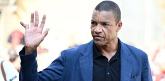 Finger That Told A Goalkeeper’s Story: Why Dida’s Hand Stole Spotlight At Franco Baresi’s Funeral Man in a blue blazer and black polo raises his right hand in a wave, outdoors, with a focused expression.