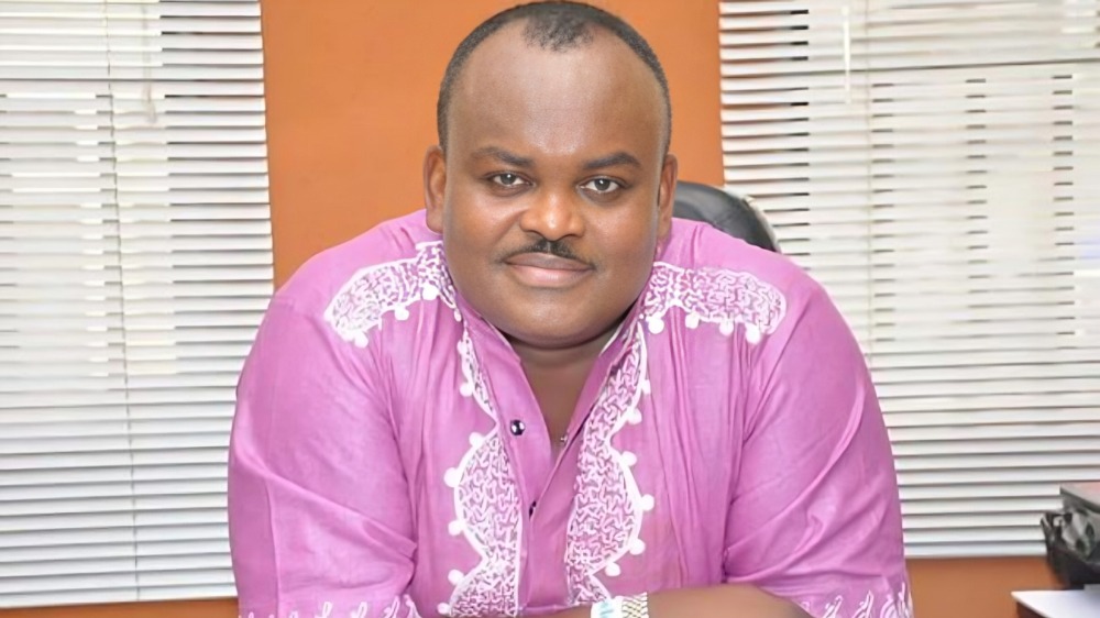 Akiyesi Solomon - THEWILL NEWS MEDIA Man seated at a desk in an office, wearing a pink traditional shirt with white embroidery, looking at the camera with a slight smile.
