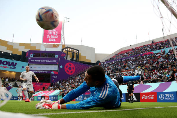 DIDA - THEWILL NEWS MEDIA Football goalkeeper in blue dives to block a ball near the goal as fans watch from the stadium stands.