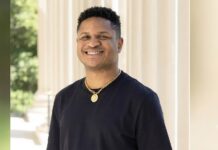 Nigerian Author’s $2 Million Dream Deal Collapses Under AI Scrutiny Smiling man in a black shirt with a gold chain stands beside columned architecture outdoors.