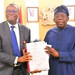 Tinubu Receives ICPC Report On Fake Presidential Agency Two men in an office exchange a document; one in a gray suit and blue tie, the other in blue traditional attire, smiling.",