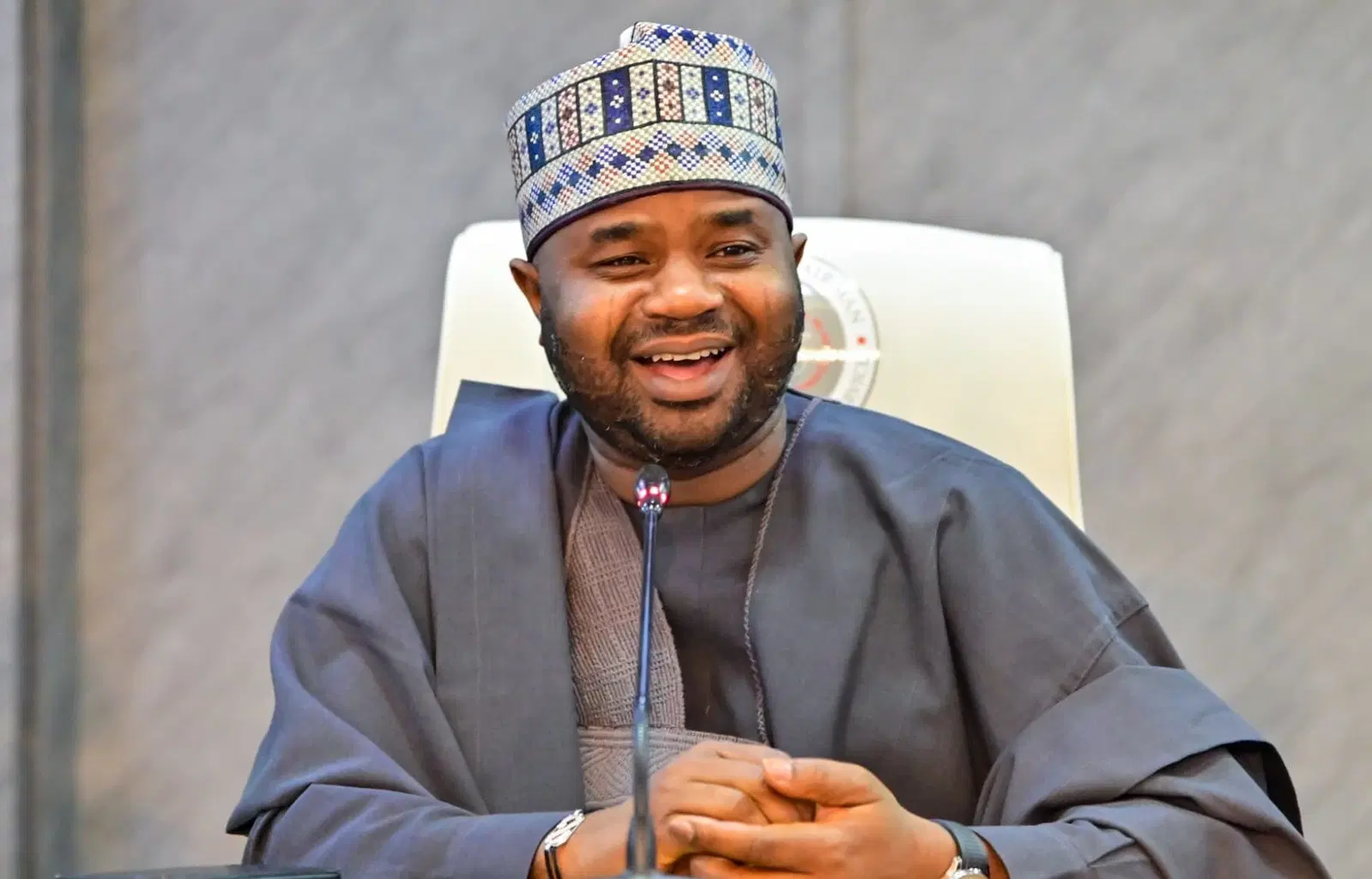 Smiling man in traditional attire with a patterned cap speaking into a conference microphone.